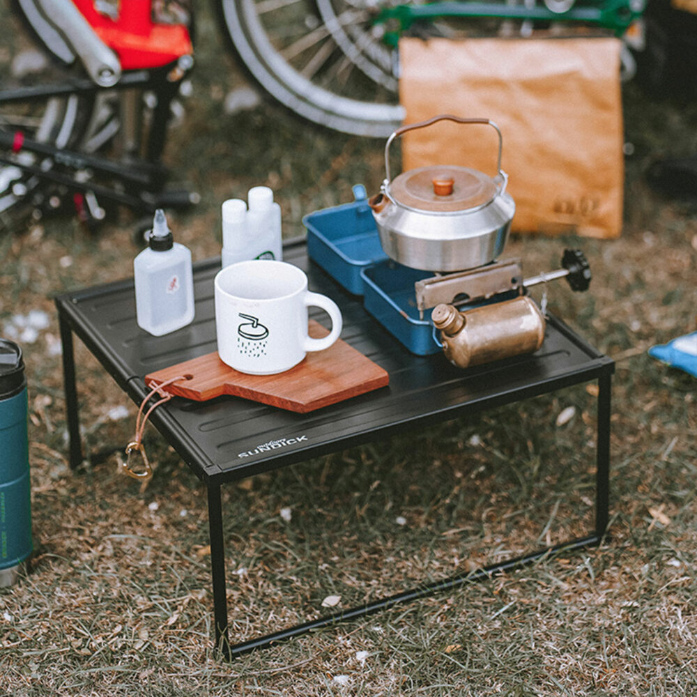 Table d'appoint pliante et portable multifonctions en alliage d'aluminium avec des objets dessus sur fond d'herbe séchée et de vélos